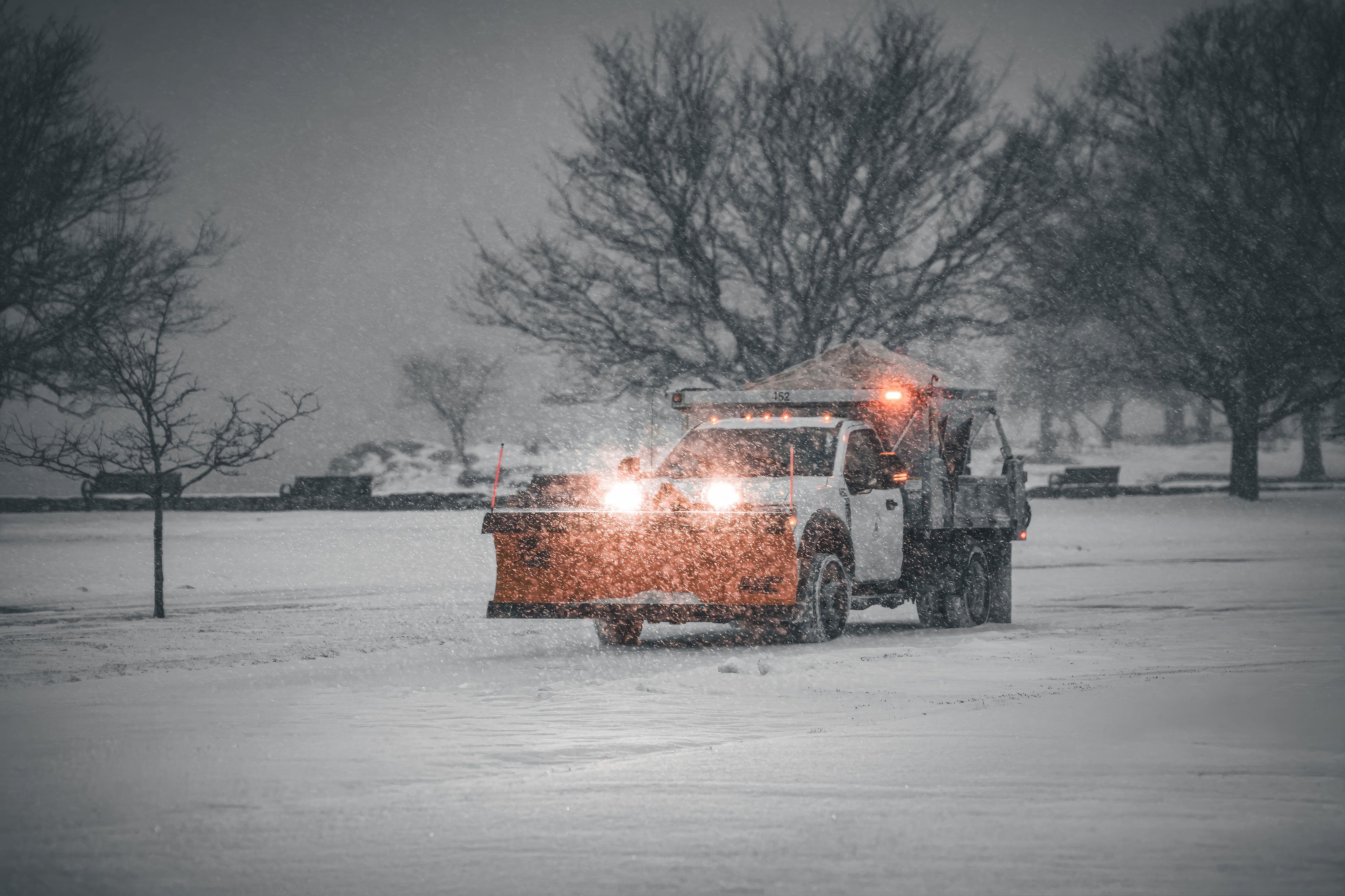 Snow plow truck clearing a commercial lot during a snowstorm